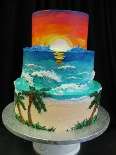 a three tiered cake decorated with palm trees and the sun setting on the beach