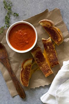 grilled cheese and tomato soup on a piece of paper next to a wooden spoon