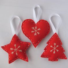 three red christmas ornaments hanging from white ribbons on a table with one heart shaped ornament and the other decorated like a snowflake