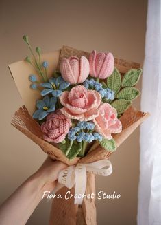 a hand holding a bouquet of flowers made out of crocheted yarn and paper