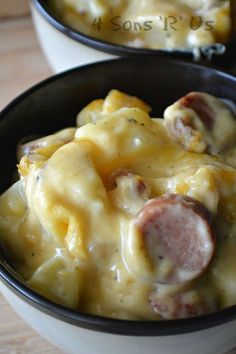 two bowls filled with macaroni and cheese covered in sausages on top of a wooden table