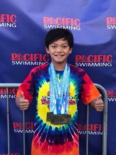 a young boy wearing a tie - dyed shirt and medal around his neck standing in front of a blue backdrop