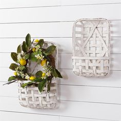 two white wicker baskets with lemons and greenery hanging on the wall next to each other