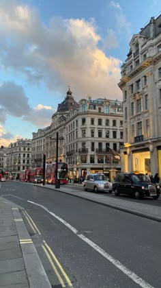 a city street with cars parked on both sides and buildings in the background at sunset