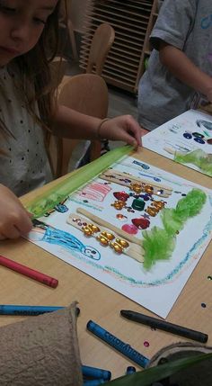 two children are sitting at a table working on their art project with crayons and colored pencils