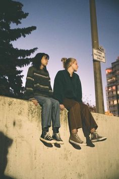 two young women sitting on top of a cement wall next to a street sign at night