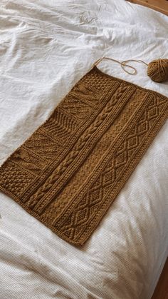 a brown knitted rug on top of a white bed