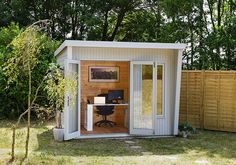 a small shed with a desk in the corner and trees behind it, on grass