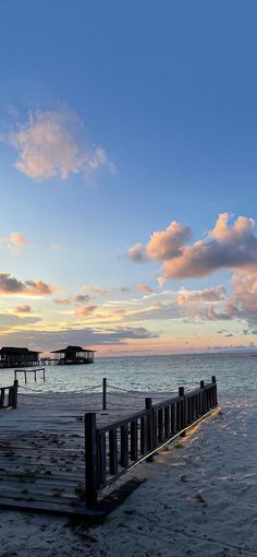 an empty pier on the beach at sunset with clouds in the sky and water behind it