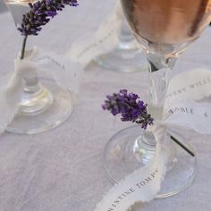 two wine glasses with flowers in them sitting on a tablecloth covered place setting for an event