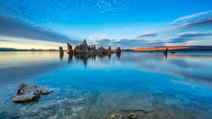 the water is crystal blue and clear with rocks in it's foreground, as the sun sets