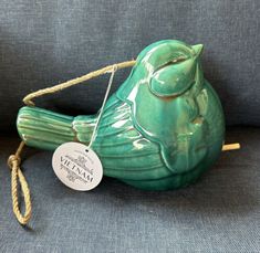 a green ceramic bird sitting on top of a blue couch next to a white tag