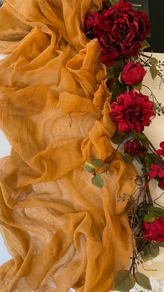 some red flowers are laying on a white table cloth and next to it is a yellow scarf