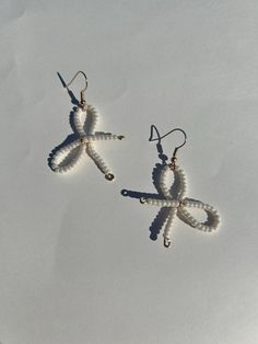 two pairs of white beaded dragon earrings on top of snow covered ground with one dangling from the ear