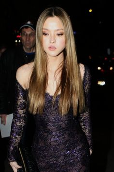 a woman with long hair wearing a purple dress and carrying a black purse in her hand