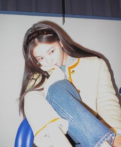 a woman sitting in a blue chair with her hand on her chin and looking at the camera