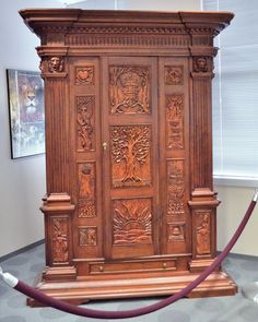 an ornate wooden cabinet is on display in a museum setting with a red hose connected to it