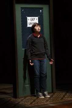 a woman standing in front of a green door with a sign on it that says gay university