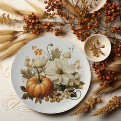 a white plate with flowers and pumpkins on it next to some dried wheat stalks