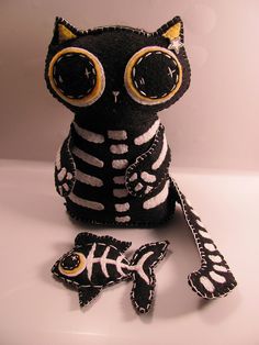 a black and white stuffed animal with yellow eyes sitting next to a small toy fish