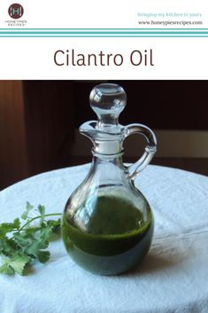 a glass bottle filled with green liquid sitting on top of a white table cloth next to a sprig of cilantro