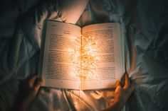 a person laying in bed reading a book with their hands on top of the book