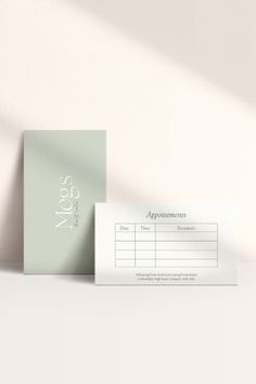 two business cards sitting next to each other on top of a white table with a plant in the corner