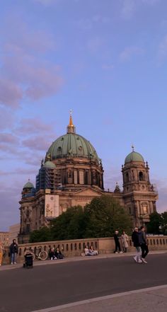 people are walking on the sidewalk in front of a large building with green dome tops