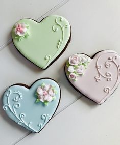 three decorated heart shaped cookies sitting on top of a white table next to each other