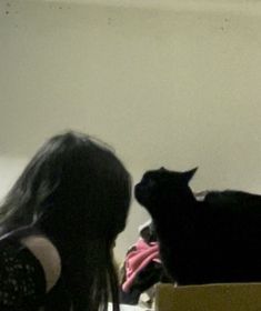 a black cat sitting on top of a box next to a woman's head