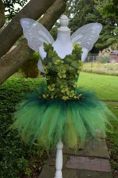 a green tutu skirt with white wings and flowers on the top, sitting in front of a tree