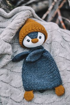 a knitted penguin wearing a blue scarf and hat on top of a white blanket