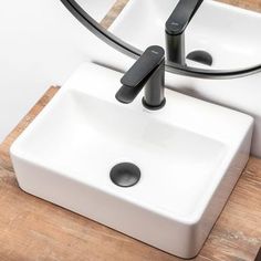 two white sinks sitting next to each other on top of a wooden table with black handles