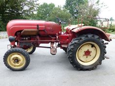 an old red farmall tractor parked in a parking lot with two large tires on the front