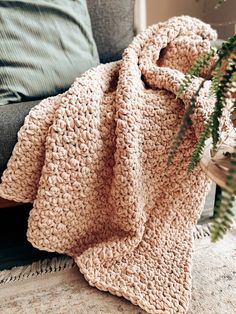 a crocheted blanket sitting on top of a couch next to a plant