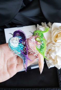 two colorful birds are sitting on someone's hand next to flowers and a card