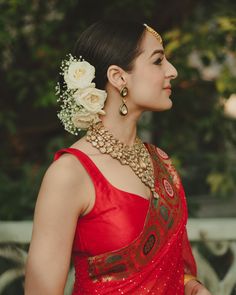 a woman wearing a red sari with flowers in her hair and jewelry on her neck