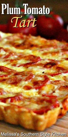 a close up of a pizza on a wooden table with tomatoes in the background and text that reads plum tomato tart