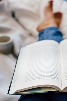 an open book sitting on top of a bed next to a person's feet