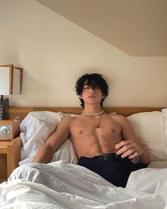 a shirtless man laying in bed with his hand on his chest and looking at the camera