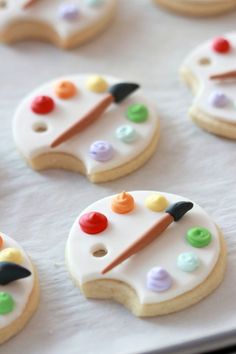 decorated cookies with paintbrushes and buttons are on a white tablecloth, ready to be eaten