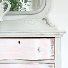 a white dresser with pink paint on it and a mirror in the corner behind it