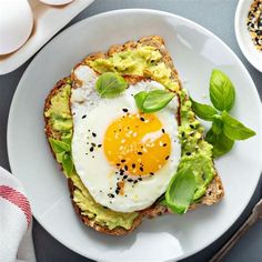 an egg and avocado toast on a white plate next to some other food