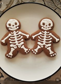 two decorated cookies in the shape of skeletons on a plate