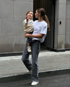 a woman carrying a child on her back while walking down the street in front of a building