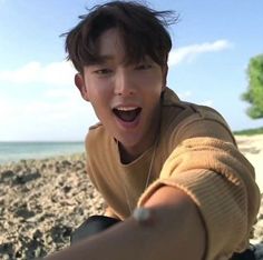 a young man sitting on top of a sandy beach next to the ocean with his mouth open