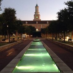 an illuminated walkway leading to a building with a clock tower in the background