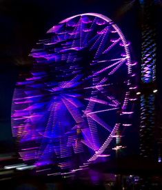 a ferris wheel lit up at night with purple lights in the dark sky behind it