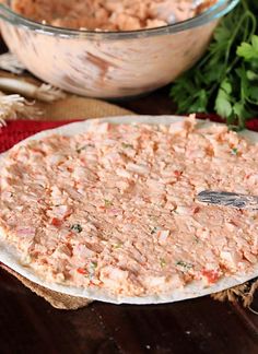 a pizza sitting on top of a wooden table next to a bowl of food and some parsley