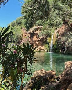 there is a small waterfall in the middle of this lake with trees and bushes around it